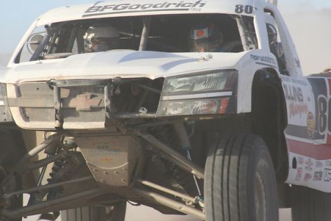 1990 Ford Bronco - white off-road race truck number 80 with BFGoodrich markings and a torn-off front fascia races through dust.