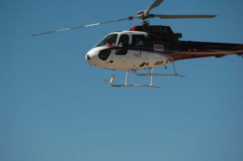 1990 Ford Bronco - white and red helicopter with SCORE markings and tail number ending 549SA hovers against a clear blue sky.