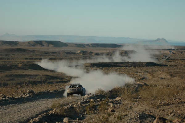 Off-road race truck raising dust on a desert course with mountains beyond