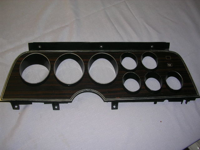 Dashboard instrument cluster bezel with woodgrain trim and multiple gauge openings