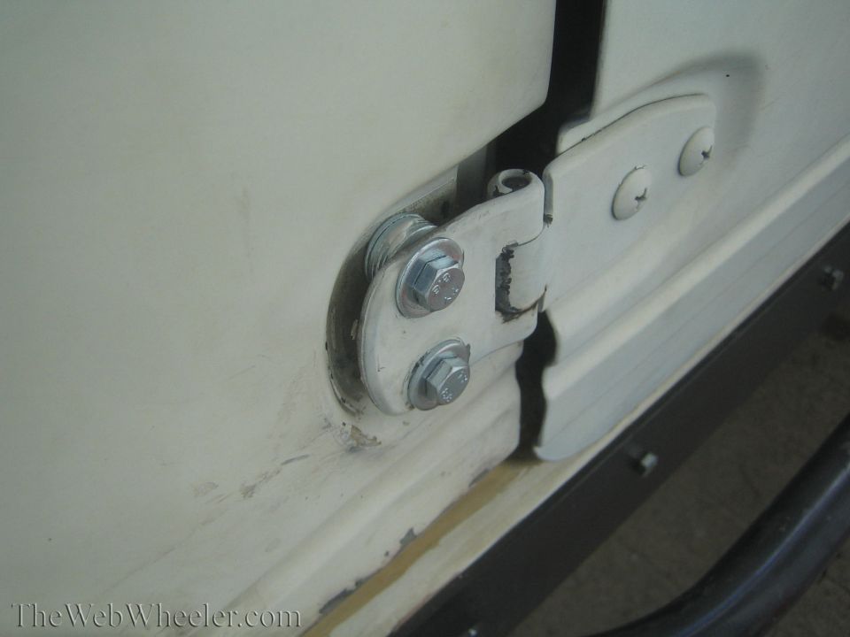 Close-up of a white door hinge with visible bolts on a cream-colored vehicle