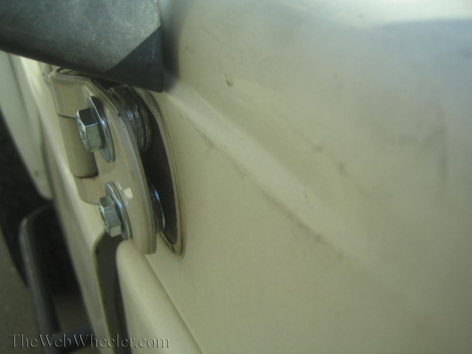 Cream-colored vehicle door hinge with visible bolts and washers