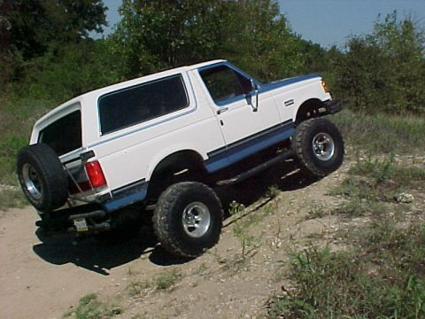 1990 Ford Bronco - This 1990 Ford Bronco is shown in a 3/4 front view, climbing a dirt incline with a spare tire mounted on the rear.