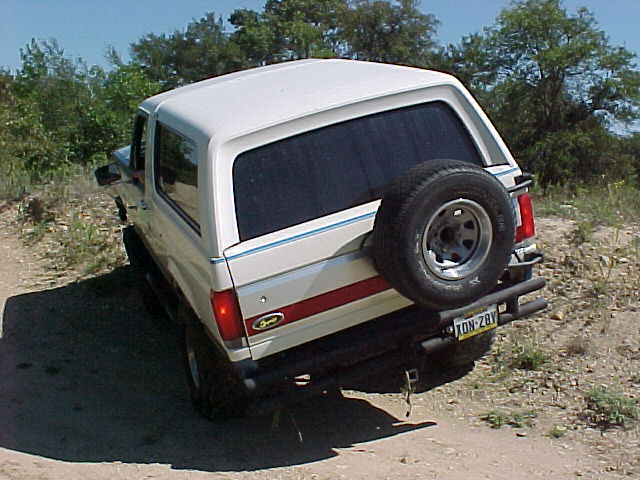 1990 Ford Bronco parked on a dirt road, rear view with spare tire mounted