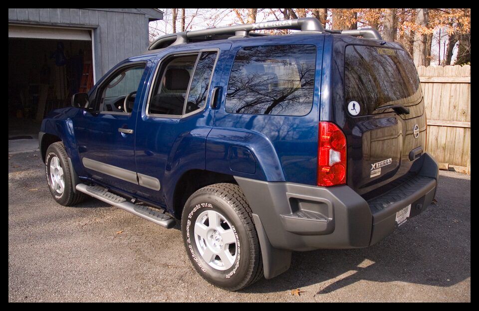 Blue 2006 Nissan Xterra parked on asphalt, with a garage behind it and trees in the background