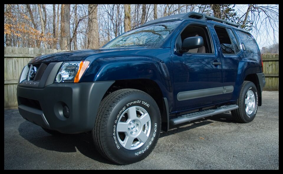 Blue 2006 Nissan Xterra parked outside with a wooden fence and trees in the background