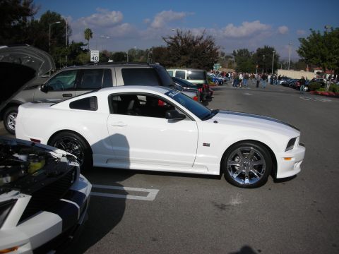 1998 Ford Crown Victoria - white late-model Mustang coupe on chrome wheels parked at a car show with other vehicles in the lot.