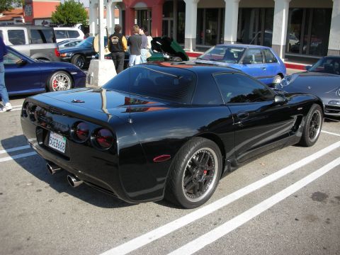1998 Ford Crown Victoria - black Chevrolet Corvette C5 coupe on dark multi-spoke wheels parked at an outdoor car meet.