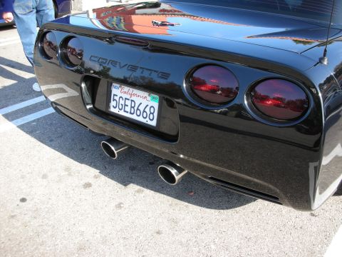 1998 Ford Crown Victoria - Close-up of a black Corvette's rear showing the Corvette badge, round taillights and a California plate reading 5GEB668.