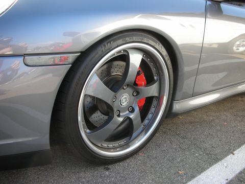 1998 Ford Crown Victoria - Close-up of a silver Porsche's front multi-spoke wheel with a chrome lip and red brake caliper.