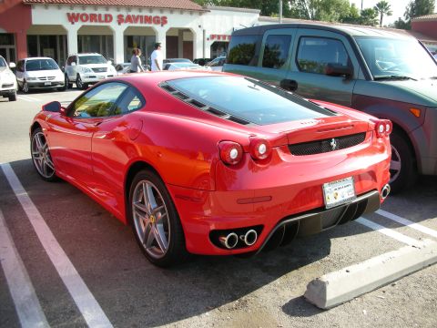 1998 Ford Crown Victoria - red Ferrari F430 coupe parked in a lot in front of a World Savings storefront, rear three-quarter view.