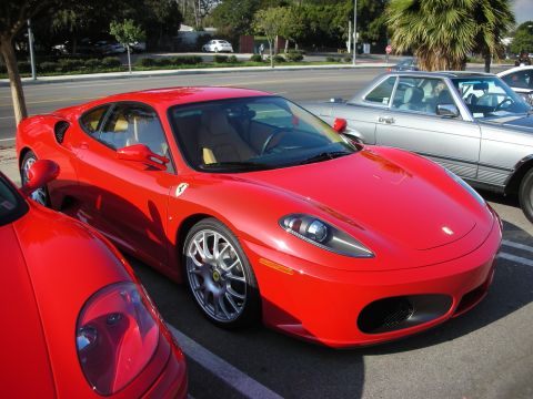 1998 Ford Crown Victoria - red Ferrari F430 coupe with multi-spoke wheels parked next to another red Ferrari in a lot.