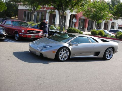1998 Ford Crown Victoria - silver Lamborghini Diablo parked in a lot with a red classic Mustang and shoppers in the background.