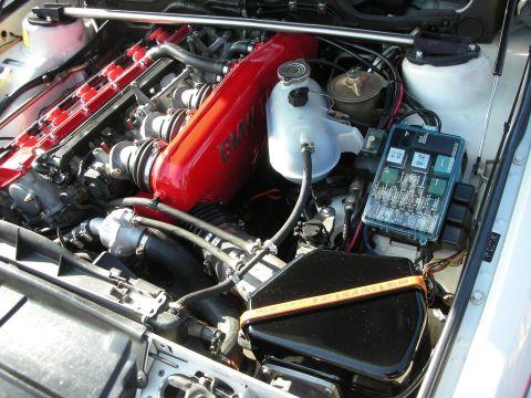 1998 Ford Crown Victoria - open BMW engine bay showing the red M valve cover, reservoir tank, fuse box and black air box.