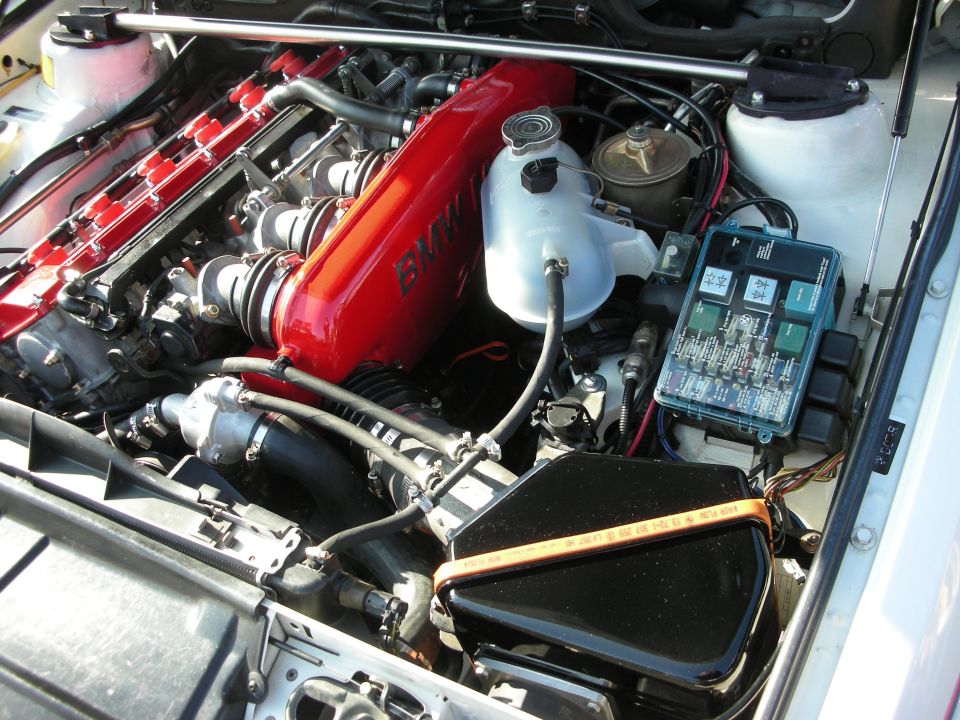 BMW engine bay showing red valve cover, fuse box and air box in white car