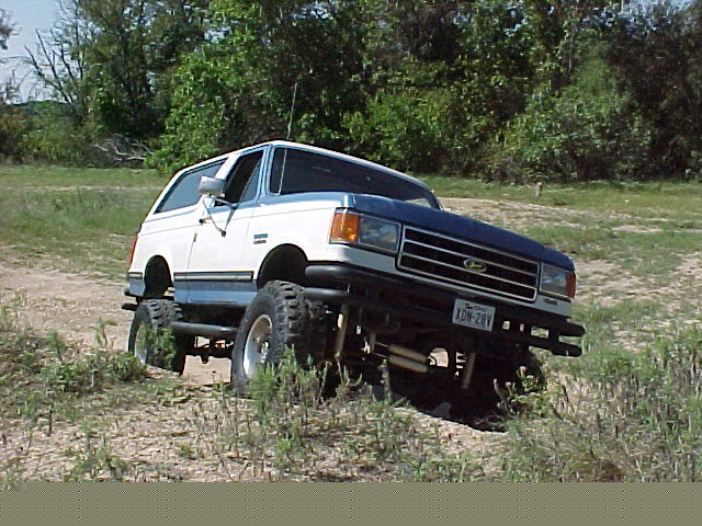 1990 Ford Bronco, 3q-front view, white and blue, lifted for off-roading. License plate XON-28V