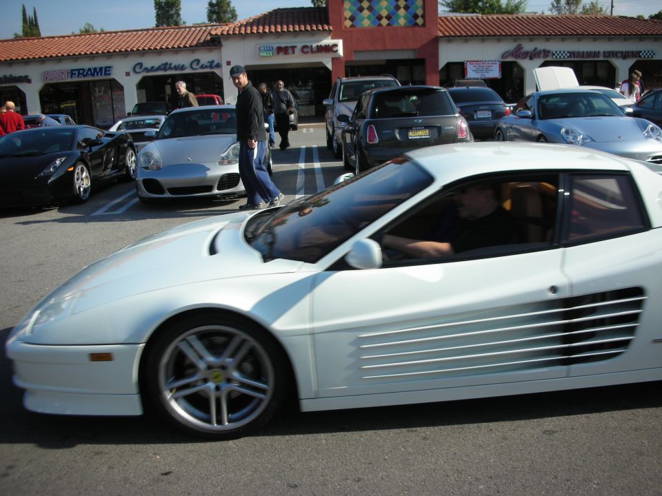 White Ferrari Testarossa with side strakes driving through a strip-mall parking lot