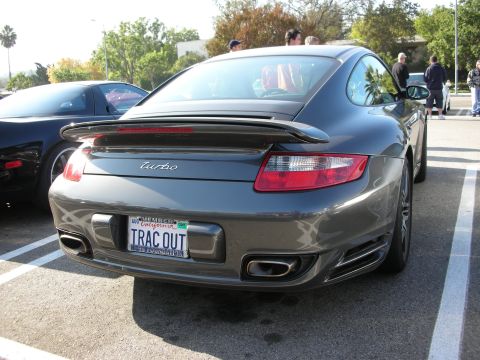1998 Ford Crown Victoria - rear of a gray Porsche 911 Turbo shows its 'turbo' script and a California vanity plate reading TRAC OUT at a car meet.