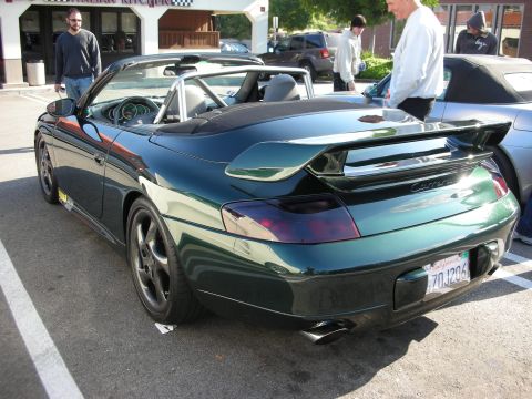 1998 Ford Crown Victoria - dark green Porsche 996 Carrera cabriolet with its rear wing extended is parked at an outdoor car meet near a restaurant.