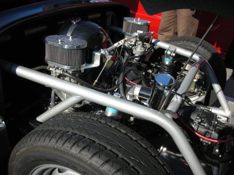 1998 Ford Crown Victoria - polished mid-mounted engine sits in a tubular frame with twin chrome air filters, behind a red body panel and exposed tires.