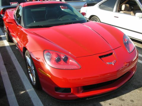 1998 Ford Crown Victoria - red Chevrolet Corvette C6 Z06 shows its crossed-flags badge and quad-headlight front end among other parked cars.