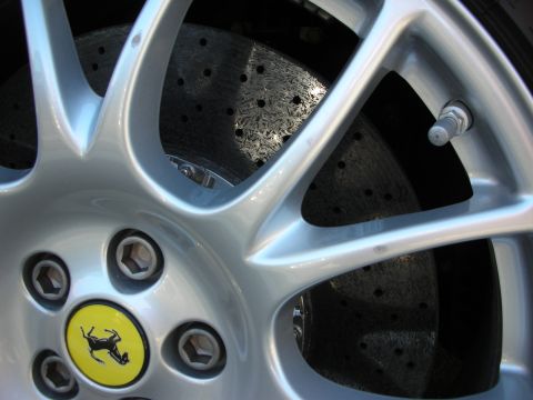 1998 Ford Crown Victoria - close-up of a silver Ferrari alloy wheel shows the yellow prancing-horse center cap and a cross-drilled brake rotor behind it.