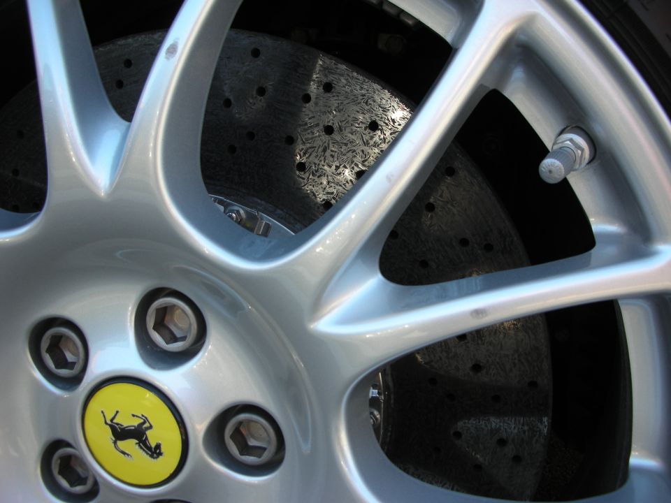 Close-up of a Ferrari alloy wheel with yellow prancing-horse cap and drilled brake rotor