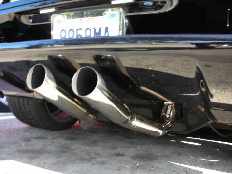 1998 Ford Crown Victoria - Two large chrome exhaust tips protrude from beneath the rear bumper of a black car, with a partly visible 2007 license plate above.