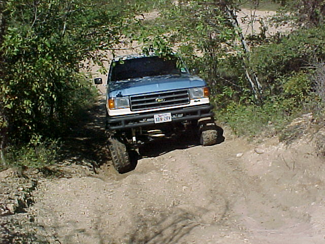 blue pickup truck going up a dirt hill with trees on both sides