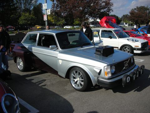 1998 Ford Crown Victoria - modified two-tone Volvo 240 coupe with a hood scoop, lowered stance and aftermarket wheels sits at an outdoor car meet.