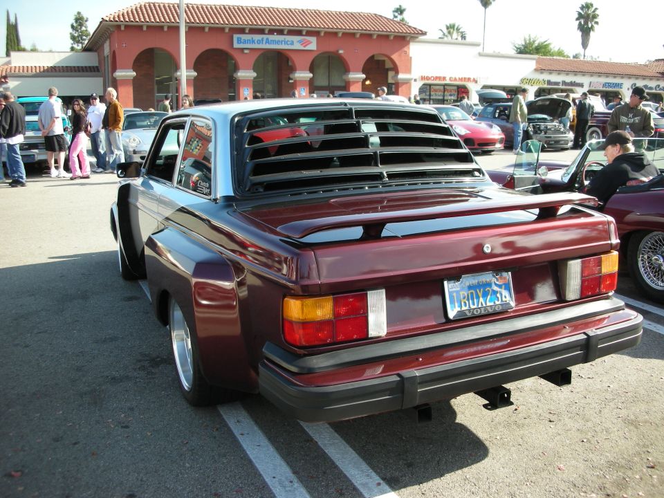 Rear of a maroon Volvo 240 coupe with rear louvers and flared fenders at a car show
