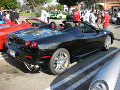 1998 Ford Crown Victoria - black Ferrari F430 Spider convertible with the top down sits among supercars at a sunny parking-lot car meet.