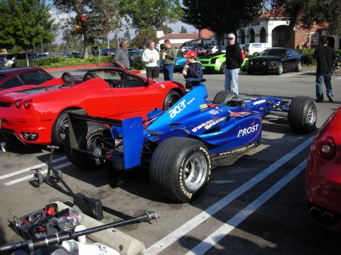 1998 Ford Crown Victoria - blue Prost open-wheel formula race car with Acer sponsorship sits on a trailer next to a red Ferrari at a car meet.