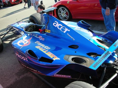 1998 Ford Crown Victoria - blue nose of a Prost formula race car covered in Acer, Bridgestone and other sponsor decals sits beside a red Ferrari at a meet.