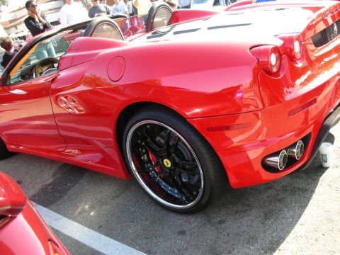 1998 Ford Crown Victoria - Side-rear view of a red Ferrari F430 Spider showing its black multi-spoke wheels, quad taillights, and twin exhaust tips at an outdoor gath…