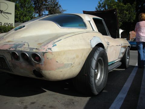 1998 Ford Crown Victoria - Rear three-quarter of a patina'd mid-1960s Corvette coupe with peeling primer paint, round taillights, and a wide rear racing tire.