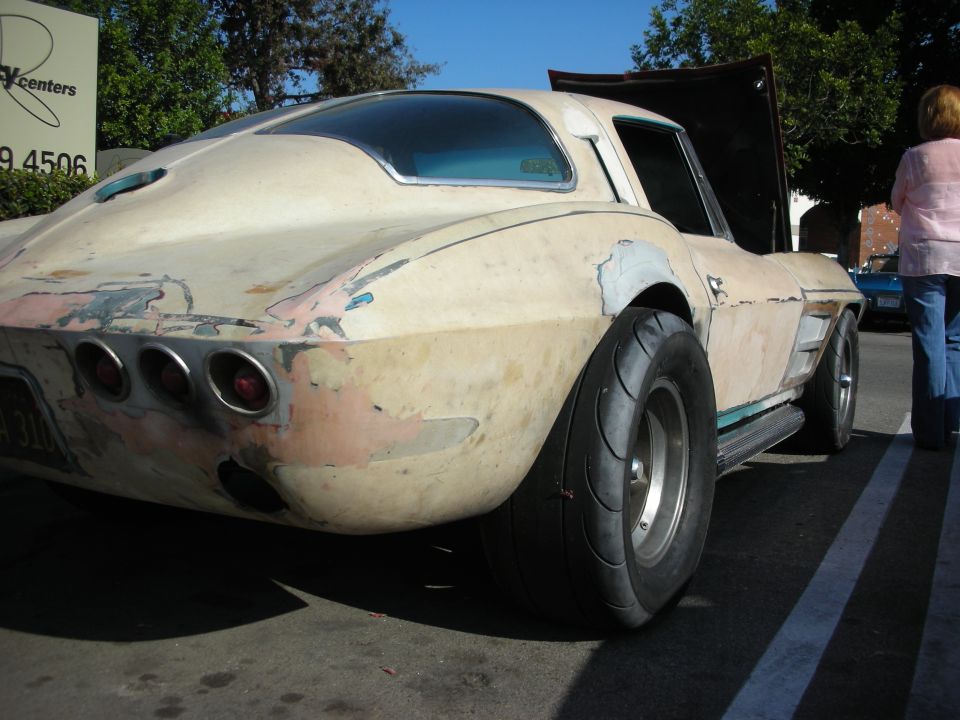 Rear of a weathered mid-1960s Chevrolet Corvette with bare patina paint and wide rear tire