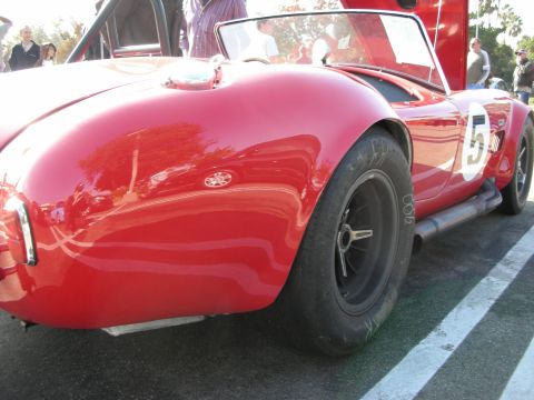 1998 Ford Crown Victoria - Rear haunch of a red Shelby Cobra roadster wearing a white roundel with the number 5, a black wire-style wheel, and a side exhaust.