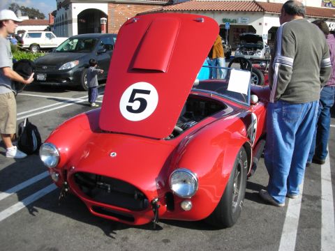 1998 Ford Crown Victoria - Front three-quarter of a red Shelby Cobra roadster with its hood propped open, twin headlights, and a white number 5 roundel.
