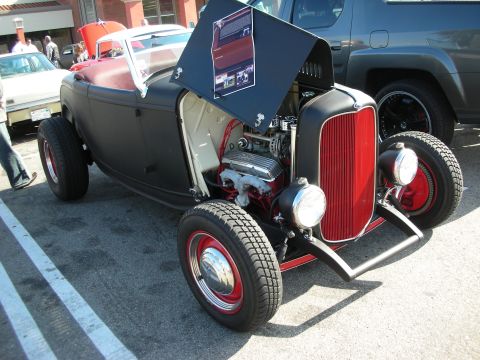 1998 Ford Crown Victoria - black '32-style highboy hot rod roadster sits with hood open, showing a chrome-topped V8, red grille shell, and red steel wheels.