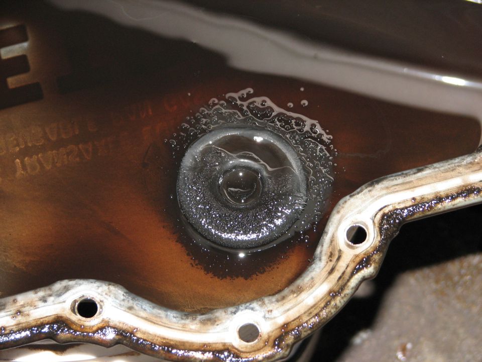 Transmission pan drain plug with foamy fluid and metal shavings, close-up