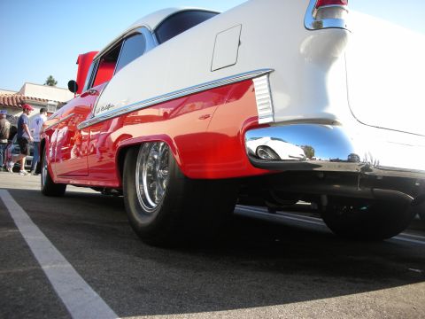 1998 Ford Crown Victoria - Low-angle rear-quarter view of a red-and-white mid-1950s Chevrolet Bel Air showing chrome trim, bumper, and polished wheels.