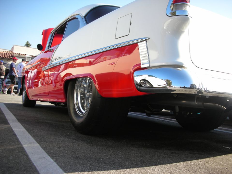 Low rear-quarter shot of a red-and-white 1955 Chevrolet Bel Air with chrome wheels