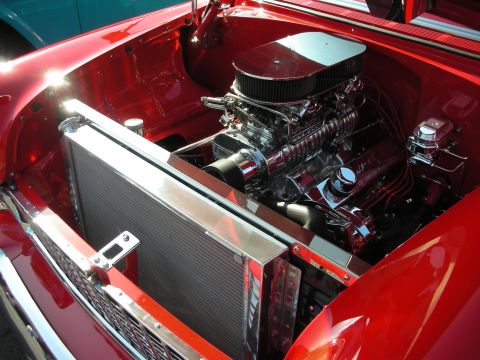 1998 Ford Crown Victoria - Engine bay of a red show car packed with a polished supercharged V8 topped by an air cleaner, beside a large aluminum radiator.