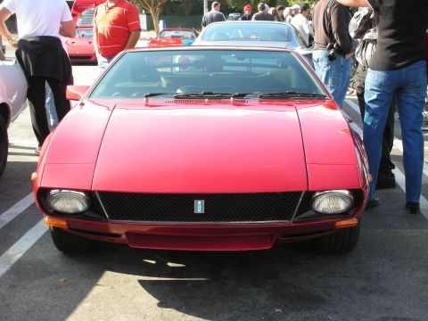 1998 Ford Crown Victoria - Head-on front view of a red wedge-shaped mid-engine Italian coupe with pop-up-style headlights and a black mesh grille, in a crowd.