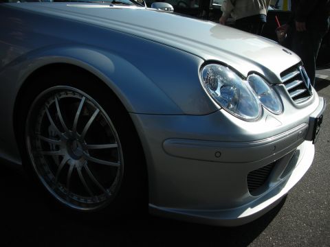 1998 Ford Crown Victoria - Low front-corner close-up of a silver Mercedes AMG coupe showing the dual headlight, star grille, front splitter, and multi-spoke wheel.