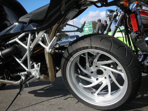 1998 Ford Crown Victoria - Close-up of a black BMW motorcycle's rear wheel, brake disc, exhaust, and silver tubular frame, with a Harley-Davidson alongside.