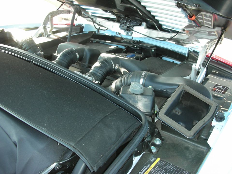 Engine bay with black intake tubing under open hood of a white car