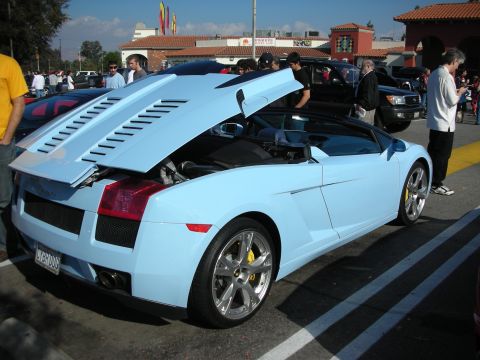 1998 Ford Crown Victoria - light-blue Lamborghini Gallardo Spyder with its rear engine cover raised, parked at a crowded car meet.