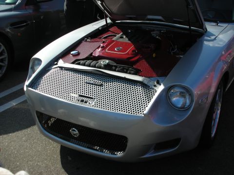 1998 Ford Crown Victoria - silver sports car shown with its hood open, revealing a red-painted engine and a mesh front grille at a car meet.